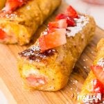 closeup of french toast roll ups with diced strawberries and powdered sugar on top