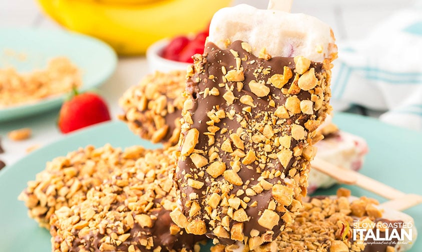 closeup of of banana split popsicles dipped in chocolate and sprinkles with chopped nuts