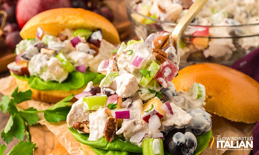 placing chicken salad with grapes and apples on a sliced roll with a spoon