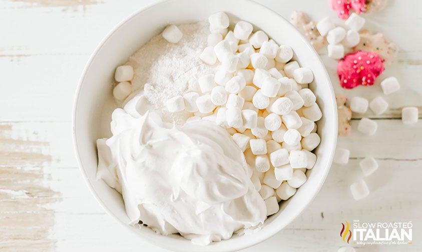 adding circus cookie fluff salad ingredients to a large white bowl
