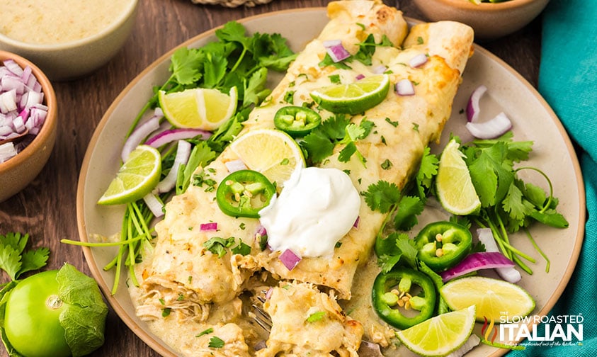 closeup of two salsa verde chicken enchiladas on a plate with a dollop of sour cream