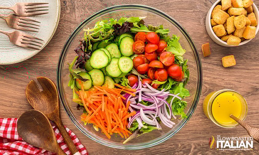 adding sliced vegetables to mixed green salad in a large bowl
