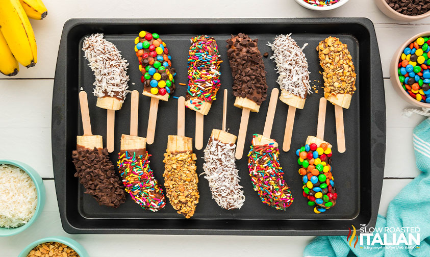 chocolate covered bananas with different toppings on sheet pan