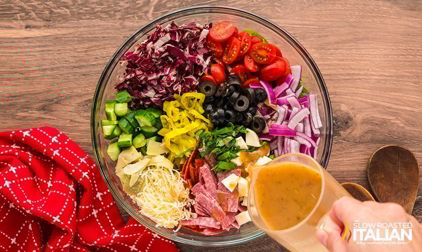 adding dressing to italian chopped salad in a large bowl