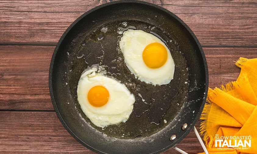 frying sunny side up eggs in a large skillet to place on a breakfast burger