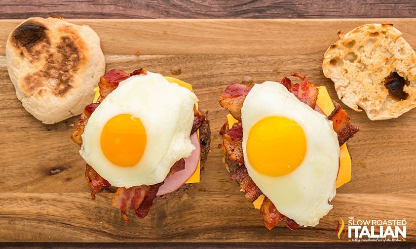stacking a breakfast burger with a burger patty, fried eggs, crispy bacon, and a slice of cheese on an english muffin