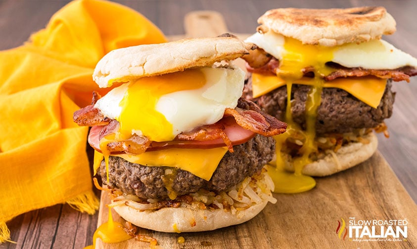 closeup of two breakfast burgers loaded with a fried egg, crispy bacon, cheese, and hashbrowns