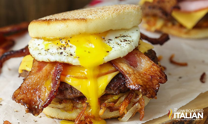 closeup of a breakfast burger loaded with a fried egg, crispy bacon, cheese, and hashbrowns