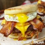closeup of a stacked breakfast burger with a runny egg, crispy bacon, hashbrown, sausage, and cheese