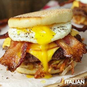 closeup of a stacked breakfast burger with a runny egg, crispy bacon, hashbrown, sausage, and cheese