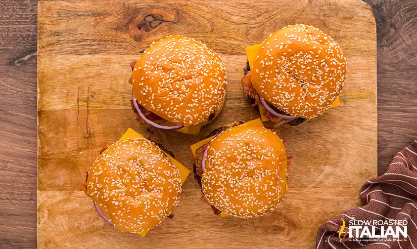 four bbq bacon burgers sitting on a wood serving board