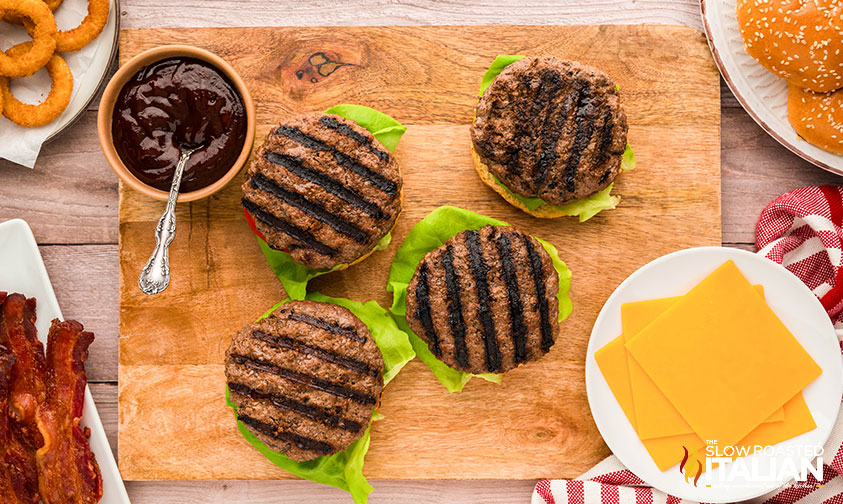 rodeo cowboy burgers on lettuce, and sliced tomato on a wooden board