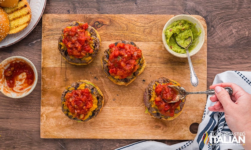 spreading pico de gallo on guacamole burger