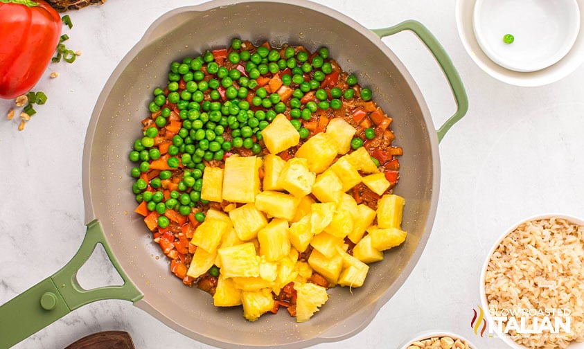 sauteed garlic and red peppers with peas, carrots, and pineapple added to the skillet for thai pineapple fried rice