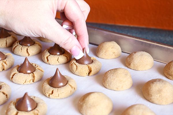 adding chocolate kisses to baked peanut blossom cookies