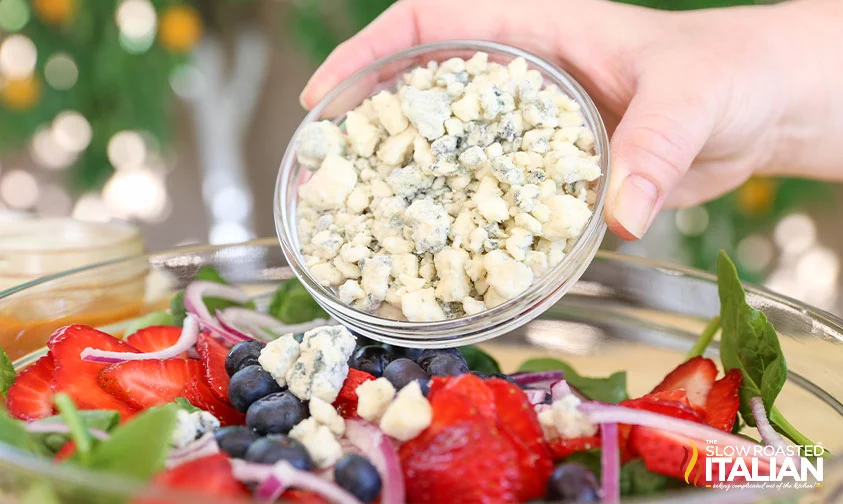 adding blue cheese to spinach strawberry salad