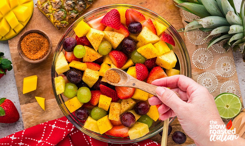adding a teaspoon of Tajin to mexican fruit salad