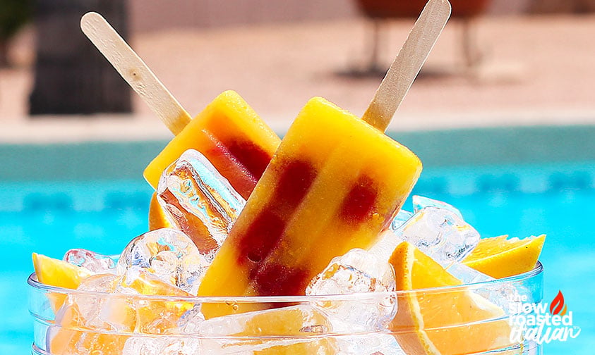 orange juice popsicles in a bowl of ice with fresh orange slices
