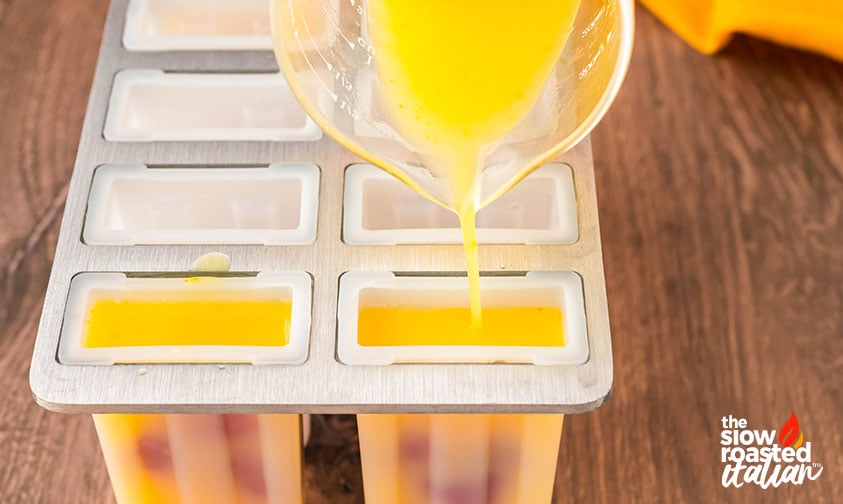 pouring orange juice popsicle mixture into mold