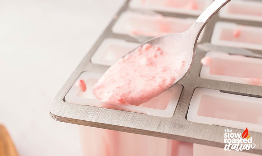 filling molds with strawberry yogurt popsicle mixture
