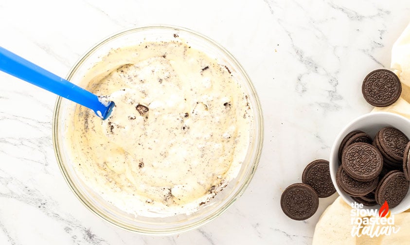 Creamy cheesecake filling with crushed Oreo pieces mixed in a bowl for Oreo cheesecake brownies