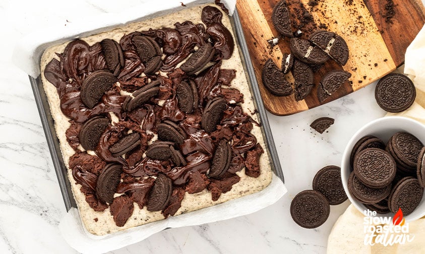 Swirled brownie batter topped with halved Oreo cookies in the pan before baking Oreo cheesecake brownies