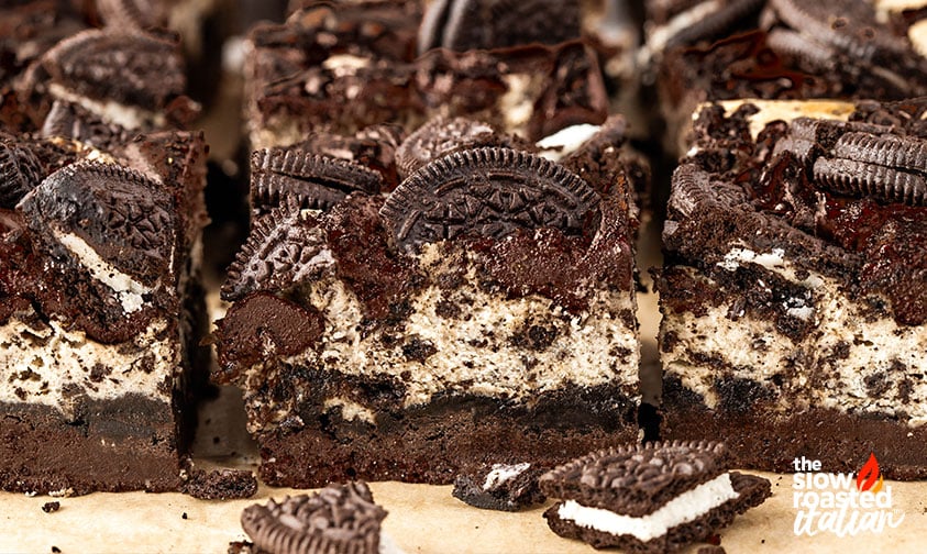 Row of sliced Oreo cheesecake brownies topped with Oreo cookie halves, showing the layered brownie and cheesecake filling