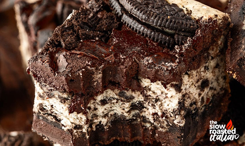 Extreme close-up of an Oreo cheesecake brownie showing the fudgy top layer and creamy cheesecake layer studded with Oreo pieces