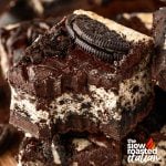 Close-up of a single Oreo cheesecake brownie square, showing the layered cheesecake and brownie stacked with crushed Oreos and a cookie on top