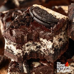 Close-up of a single Oreo cheesecake brownie square, showing the layered cheesecake and brownie stacked with crushed Oreos and a cookie on top