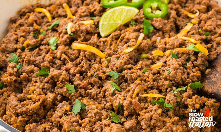 Close-up of refried bean casserole garnished with cilantro, shredded cheese, jalapeño slices, and lime