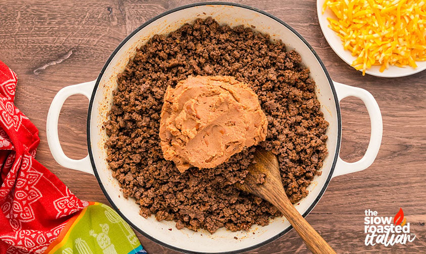 Refried beans added to browned ground beef in a pot for refried bean casserole