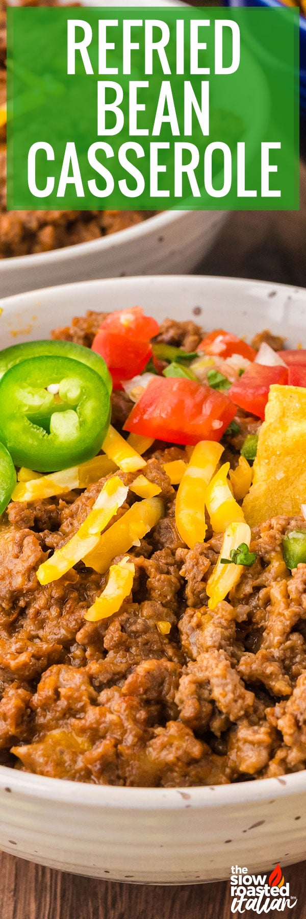 Refried bean casserole topped with jalapeños, shredded cheese, pico de gallo, and a tortilla chip in a bowl