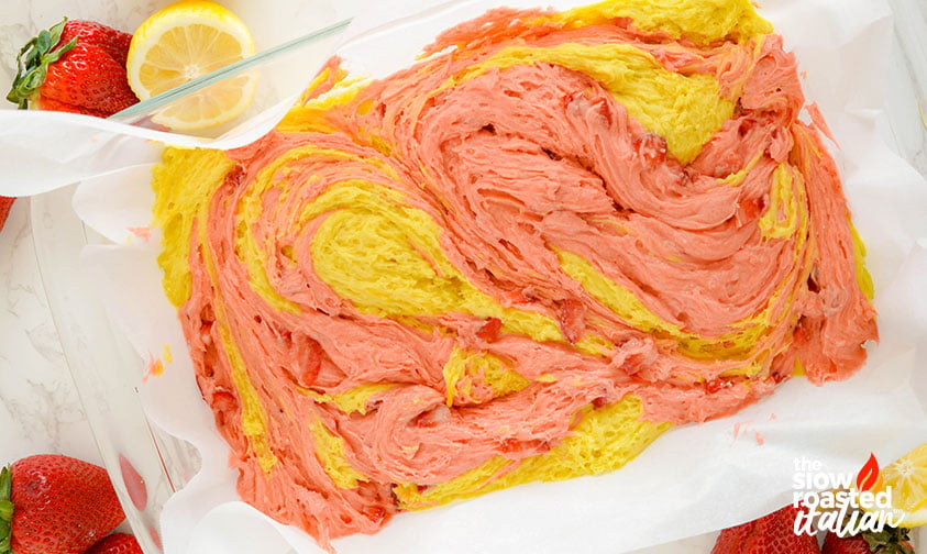 Strawberry brownie batter swirled with pink and yellow lemonade layers in a lined baking pan before baking