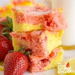 Stacked strawberry brownies with a pink and yellow lemonade swirl and white lemon glaze, garnished with fresh strawberries and lemon slices