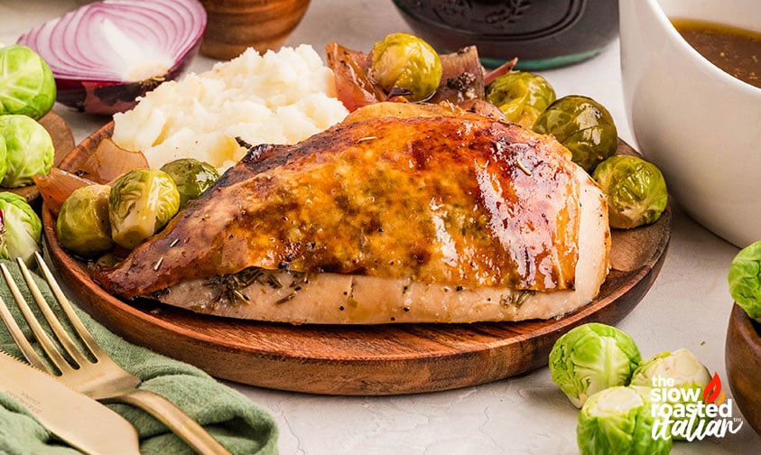 Plated roast chicken recipe served with mashed potatoes, Brussels sprouts, and gravy on a wooden plate