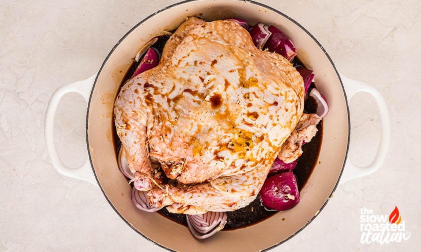 Raw chicken coated in balsamic marinade with red onion in a pot before roasting for a roast chicken recipe