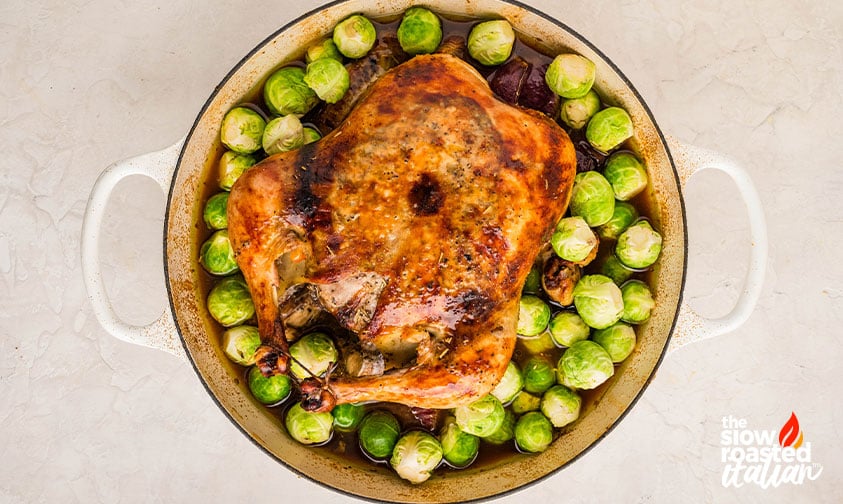 Golden roasted chicken surrounded by Brussels sprouts in a pot for a roast chicken recipe