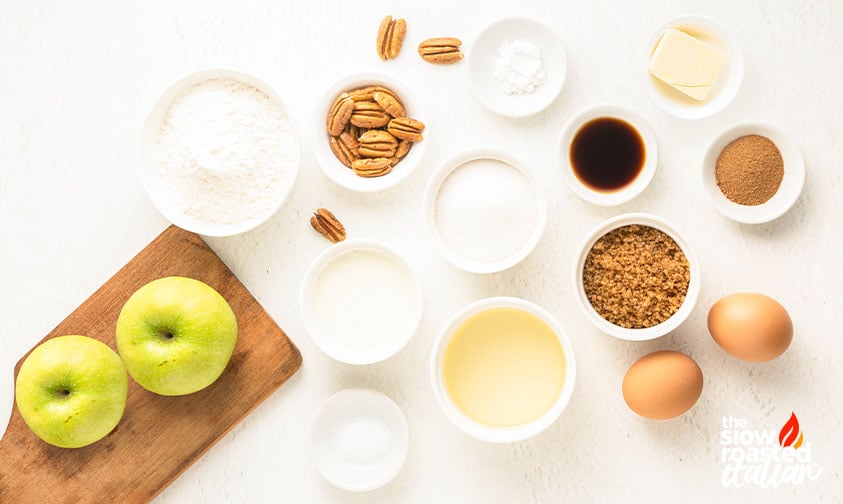 Overhead view of apple bread ingredients including green apples, flour, pecans, sugar, eggs, butter, vanilla, oil, and spices