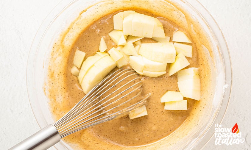 Overhead view of diced apples being folded into apple bread batter with a whisk
