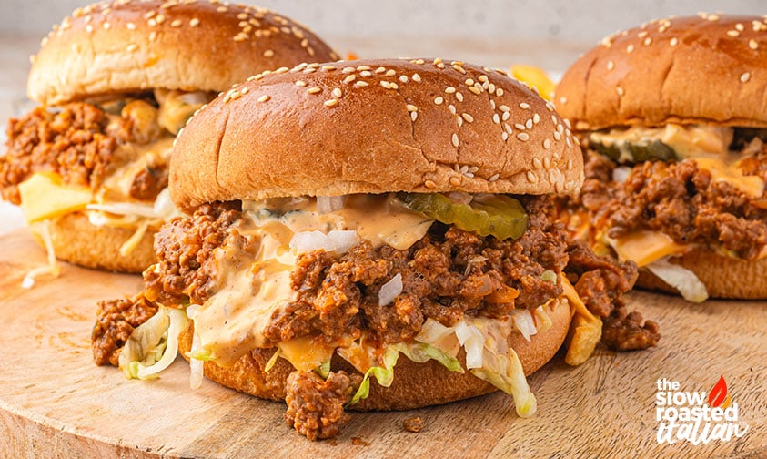 Three Big Mac sloppy joes on sesame buns piled with beef, cheese, pickles, and special sauce on a wooden board