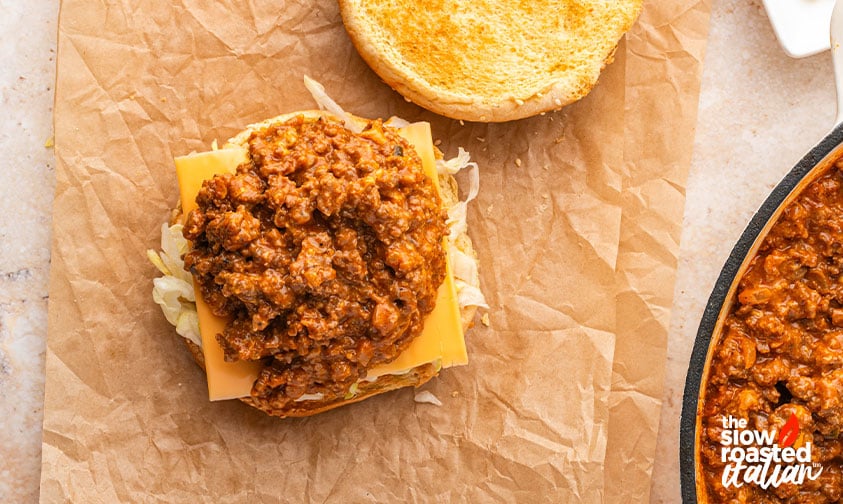 Assembling a Big Mac sloppy joe with cheese, shredded lettuce, and seasoned beef on a toasted bun
