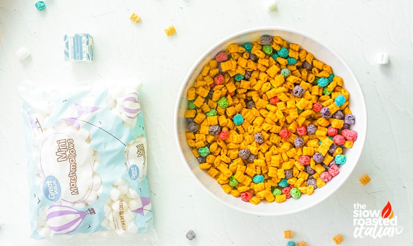 Overhead view of a bowl of colorful Cap’n Crunch cereal next to a bag of mini marshmallows and butter
