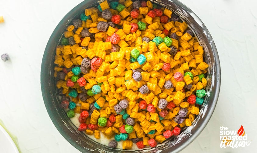 Overhead view of colorful Cap’n Crunch cereal being mixed into melted marshmallow in a pot
