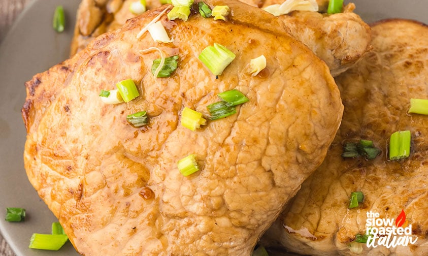 Close-up of marinated pork chops with golden caramelized edges, topped with chopped green onions