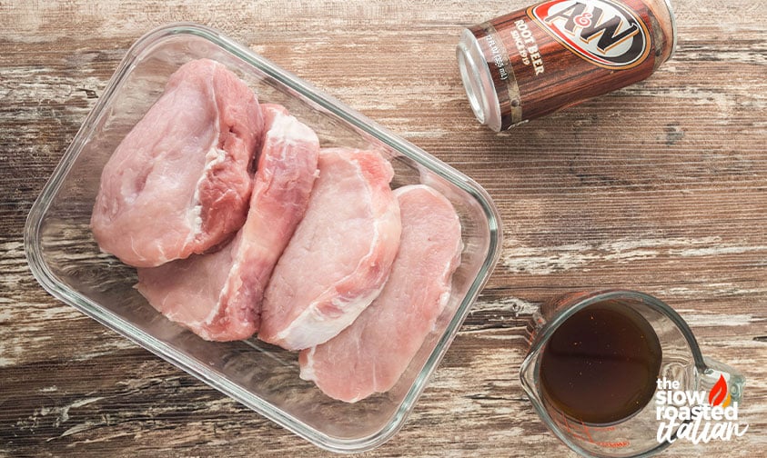 Raw pork chops in a glass dish next to root beer and marinade for marinated pork chops