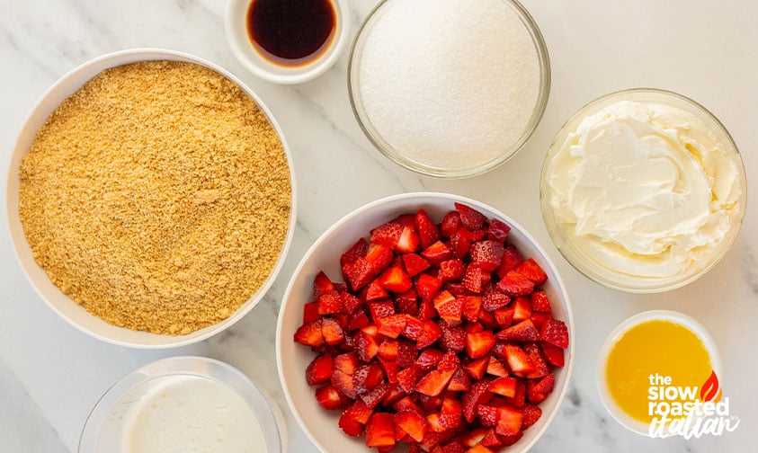 Ingredients for no bake strawberry cheesecake including graham cracker crumbs, cream cheese, sugar, diced strawberries, and melted butter