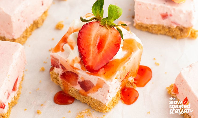 A no bake strawberry cheesecake bar showing the graham crust and fluffy pink filling