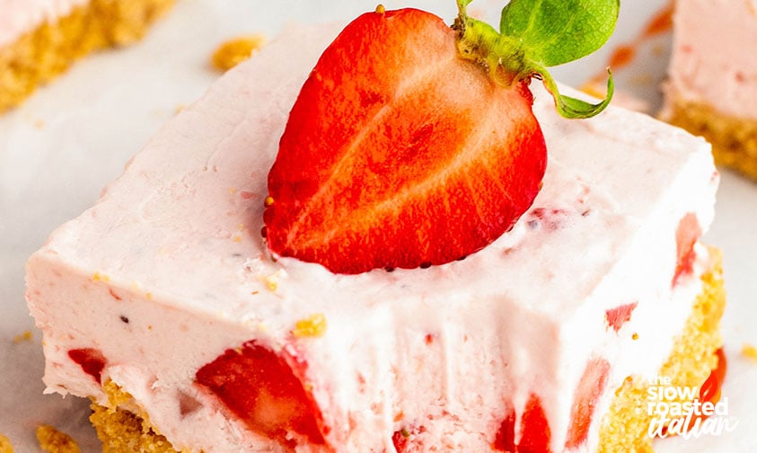 Extreme close-up of a no bake strawberry cheesecake bar topped with a fresh strawberry, showing the creamy filling and graham cracker crust