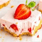 Close-up of a no bake strawberry cheesecake bar with graham cracker crust, creamy filling, and a fresh strawberry on top